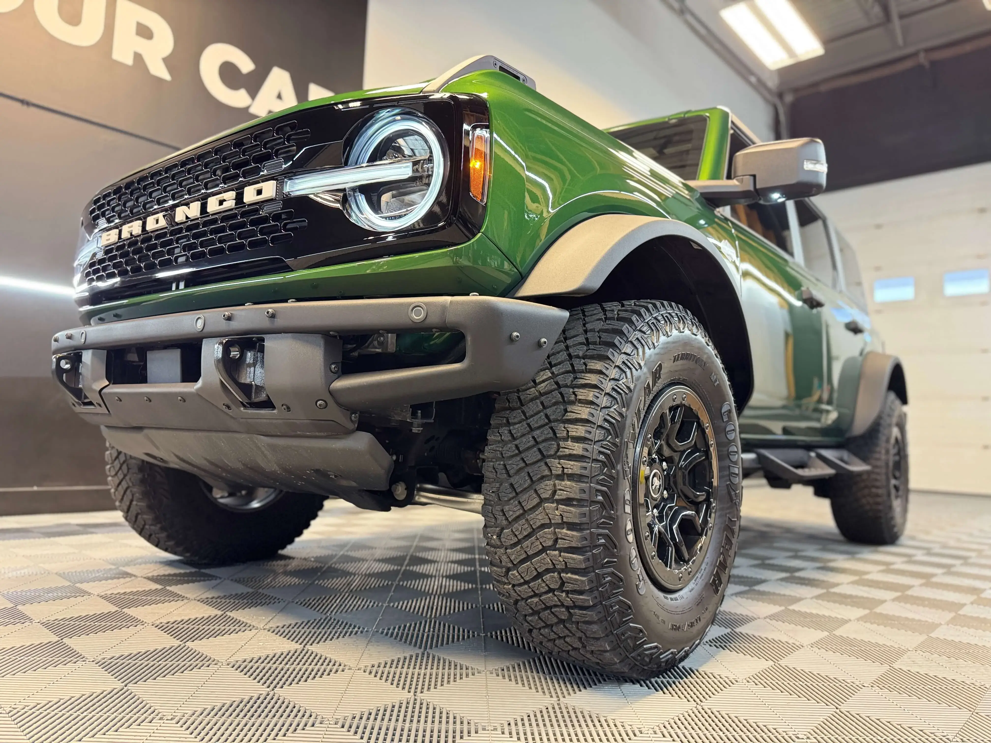 Detail Lab. Blue Volkswagen Golf R hatchback parked inside a detailing studio. The polished paintwork reflects the bright overhead lighting. The checkered flooring adds contrast.