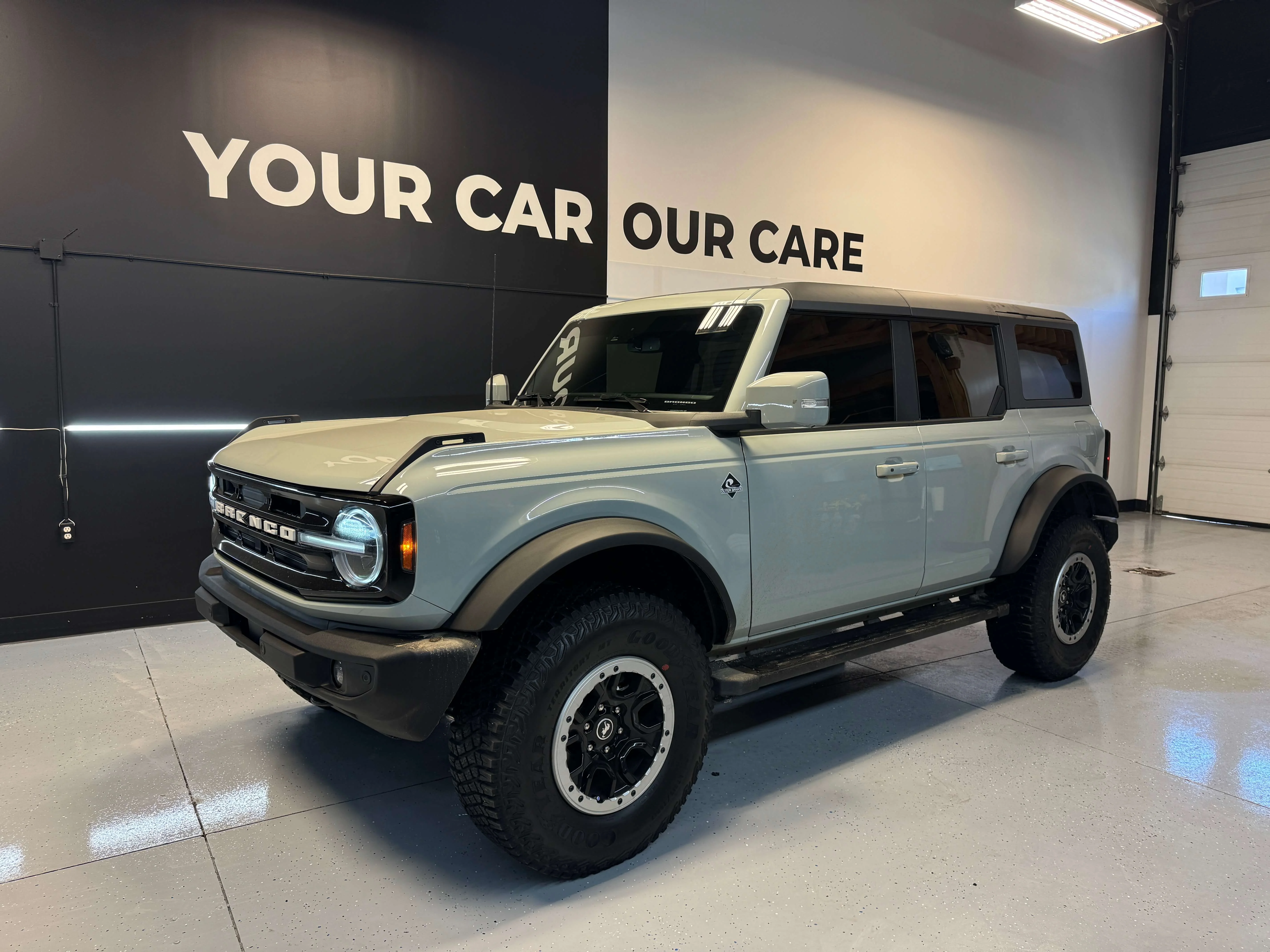 Detail Lab. Gray Ford Bronco SUV parked in a professional detailing shop with a clean, polished finish. The shop's branding, YOUR CAR OUR CARE, is displayed on the wall behind the vehicle.